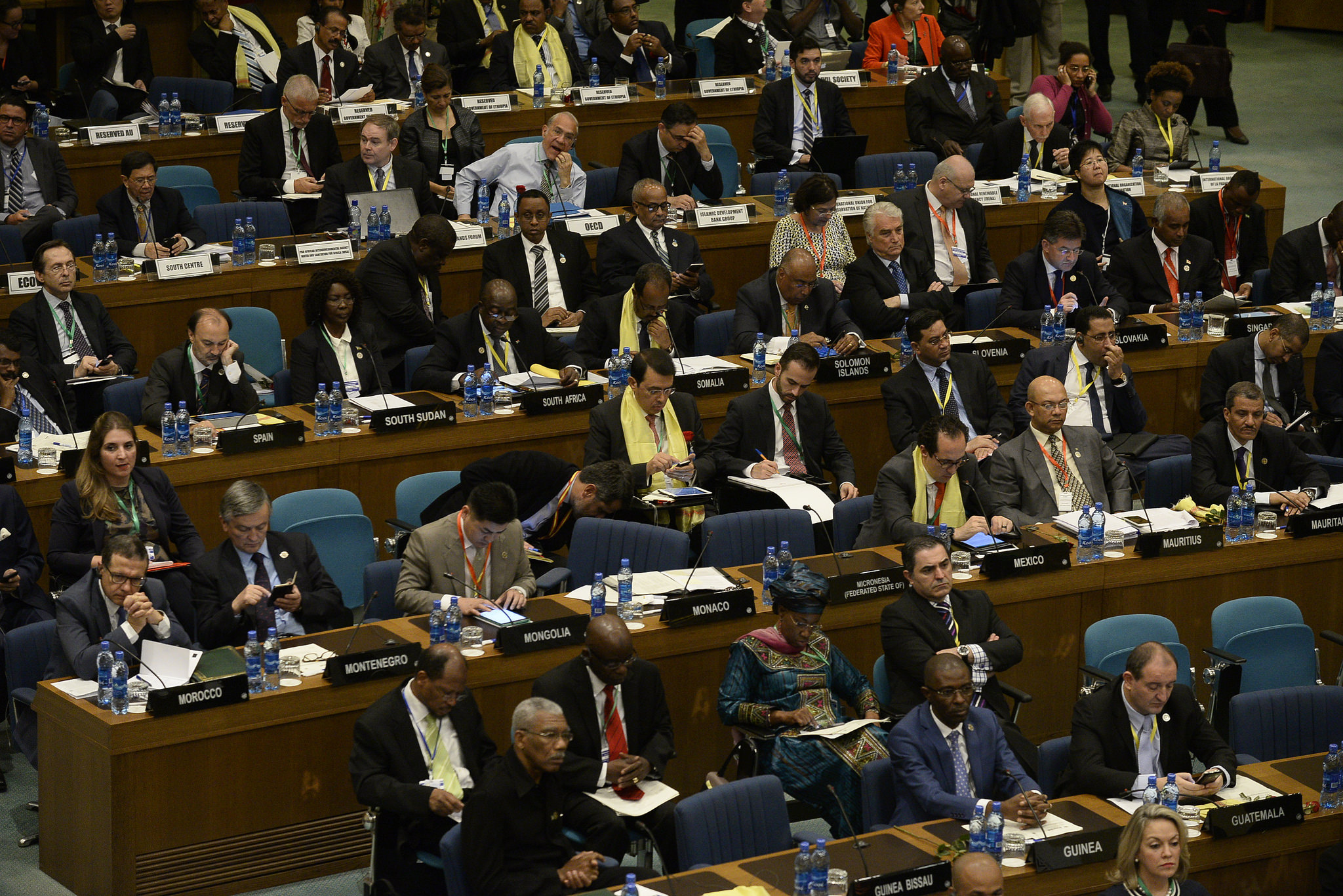 Rows of people in suits, many looking at blackberries or laptops, in the UN Conference Centre